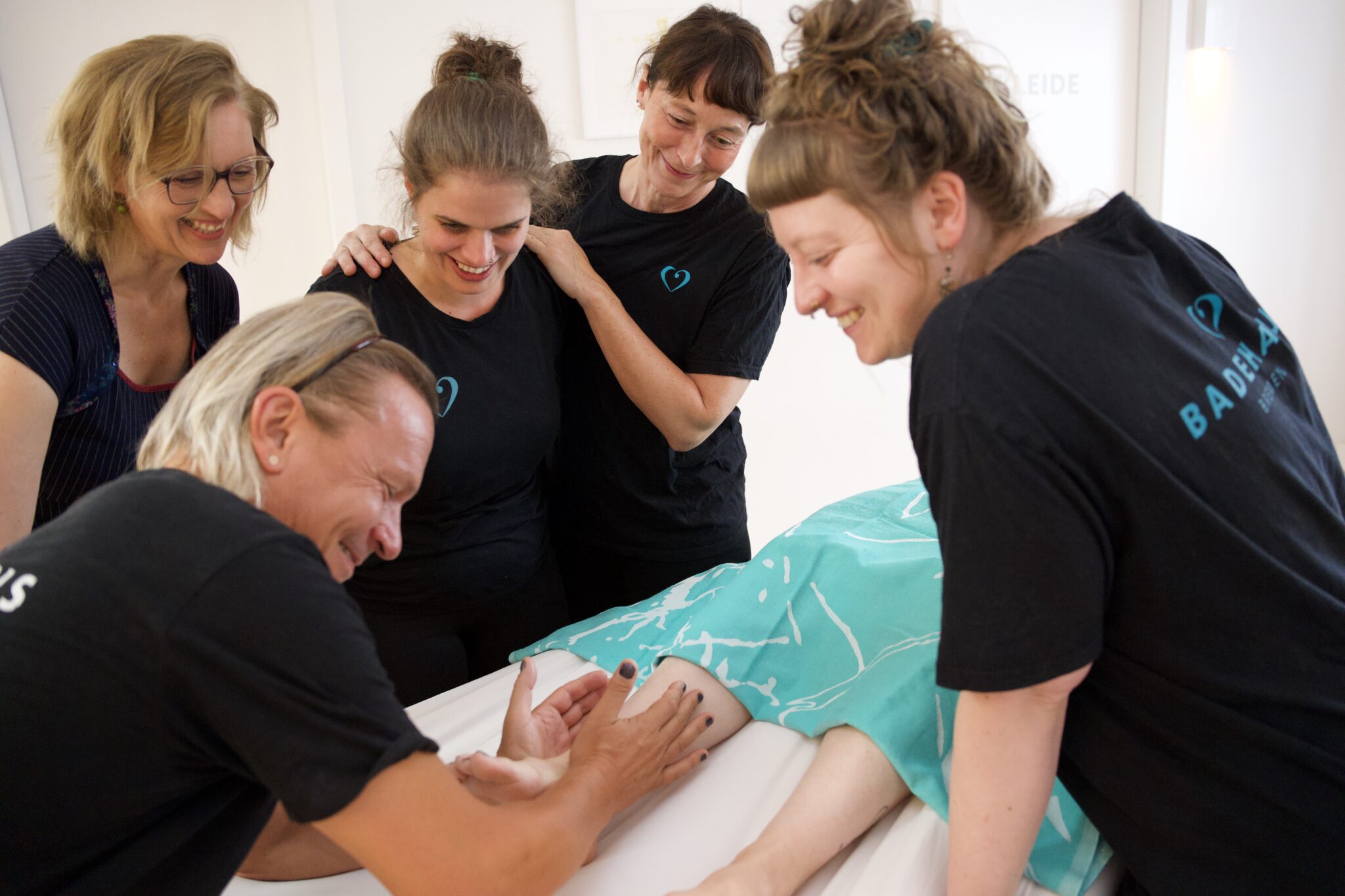 Ein Mann zeigt Massagegriffe am Fuss und vier Personen schauen zu und lernen.